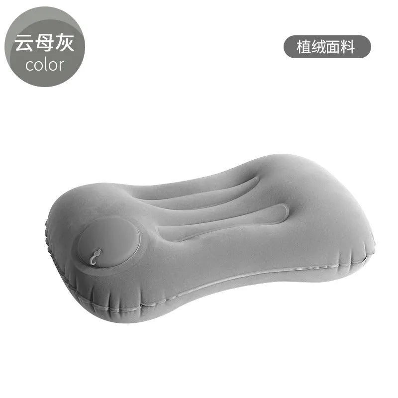 Grey inflatable travel pillow with soft flocking surface, shown deflated and next to a backpack for scale.