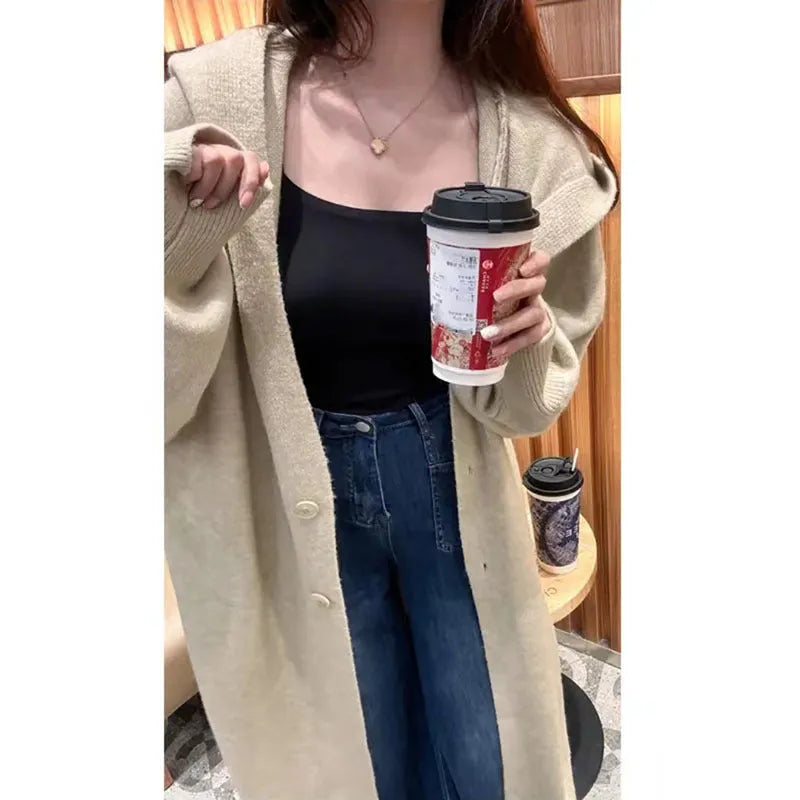 A woman wearing a long, beige, hooded knitted cardigan in a loose, below-the-knee Korean style.