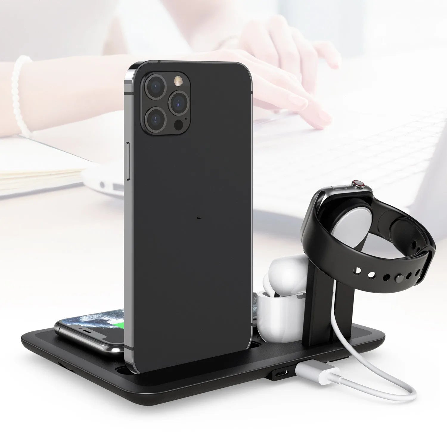 Black and white desktop wireless charging station holding a phone, watch, and headphones with a USB cable.