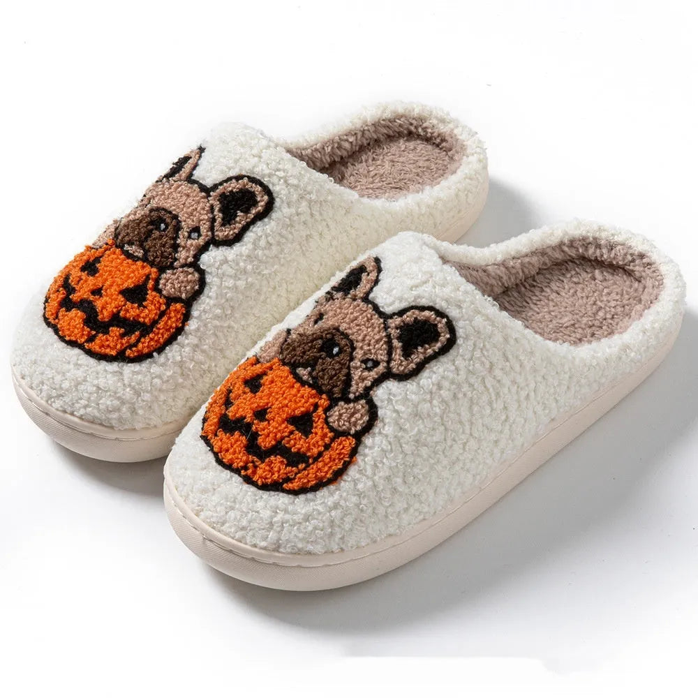 Black and white plush Halloween pumpkin slippers with textured rubber soles on a wooden floor.