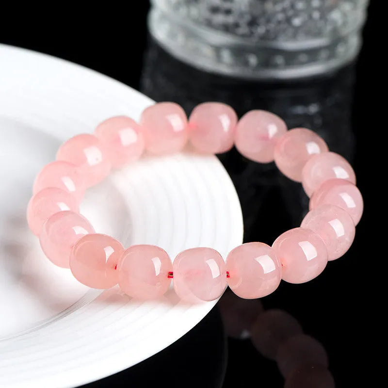 Natural pink crystal barrel bead bracelet with geometric design on a wrist.