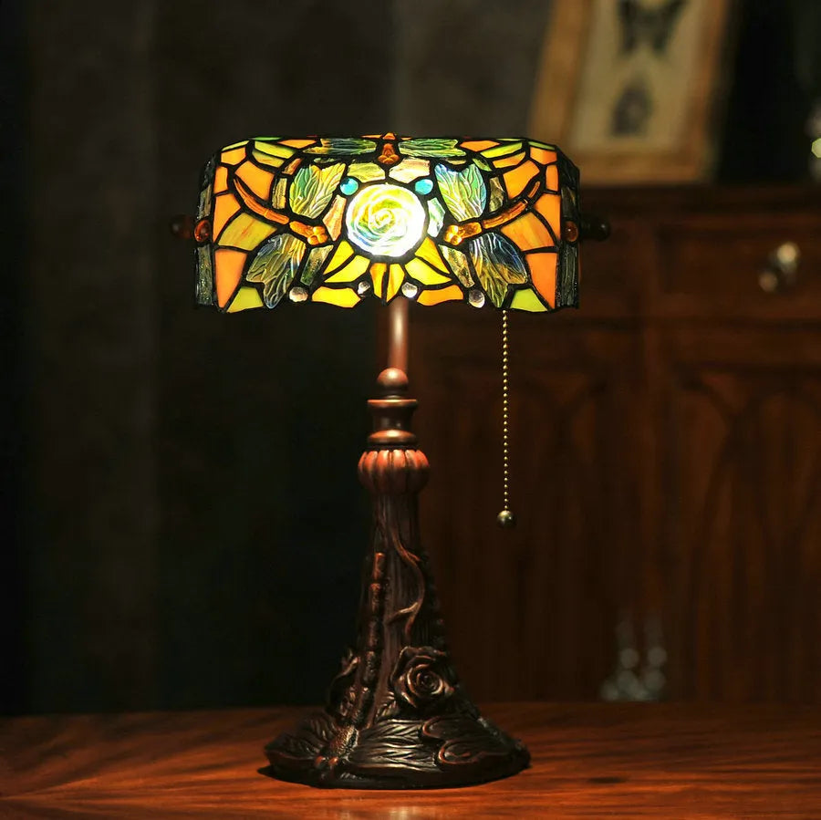 Tiffany style table lamp with colourful stained glass shade and resin base on a wooden desk