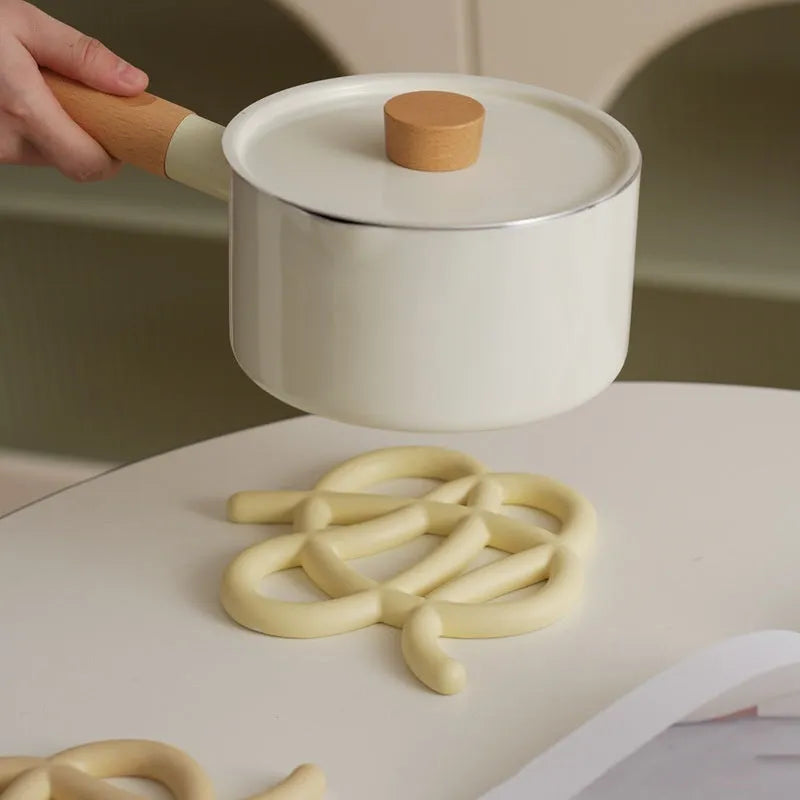 Irregular-shaped ceramic heat proof mat in grey with a curved hook for hanging, sitting on a wooden table.