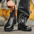 A pair of vintage-style brown Chelsea boots with a round toe and low heel on a wooden floor.