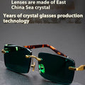 Frameless dark green crystal sunglasses with minimalist design on a case with cleaning cloth.