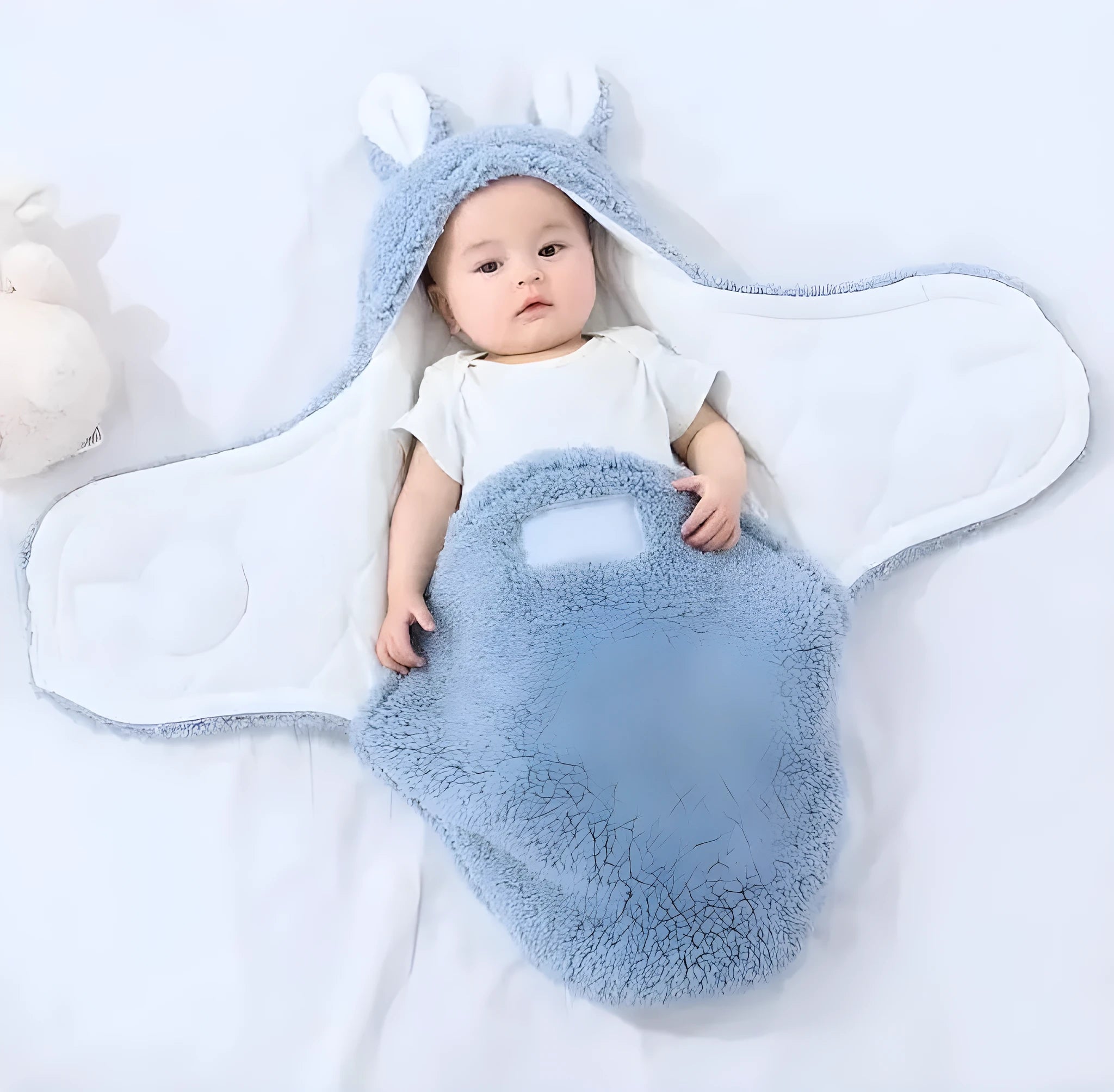 Baby wearing a blue adjustable cotton sleep sack with velcro swaddle closures and a head-protecting hood.