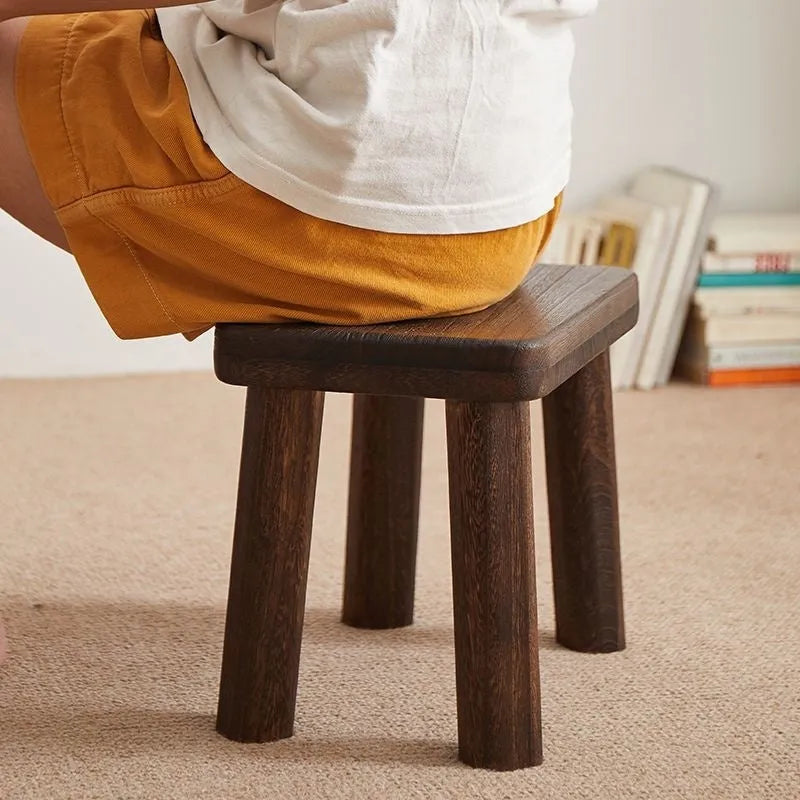 Distressed solid wood shoe changing stool with rustic bracket structure.