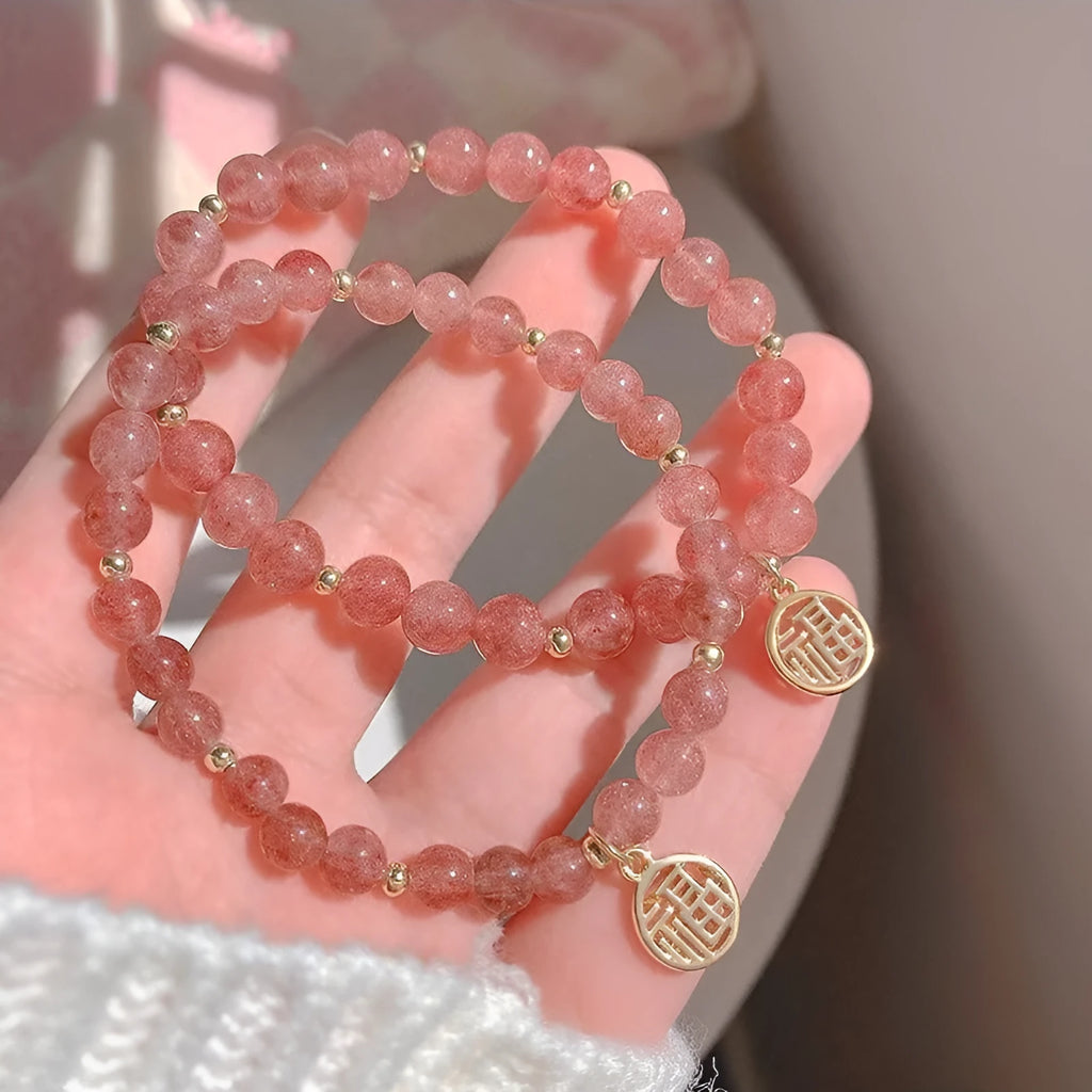 Glass strawberry quartz bead bracelet with a blessing card charm on a wrist.