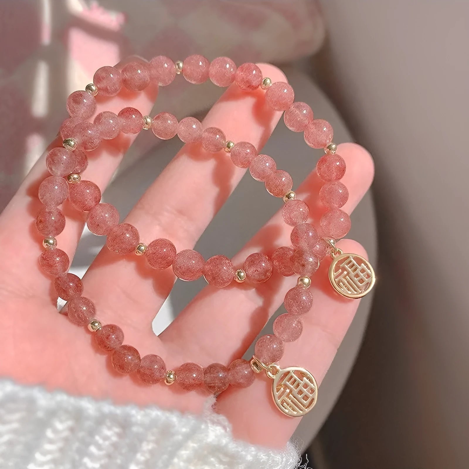 Glass strawberry quartz bead bracelet with a blessing card charm on a wrist.