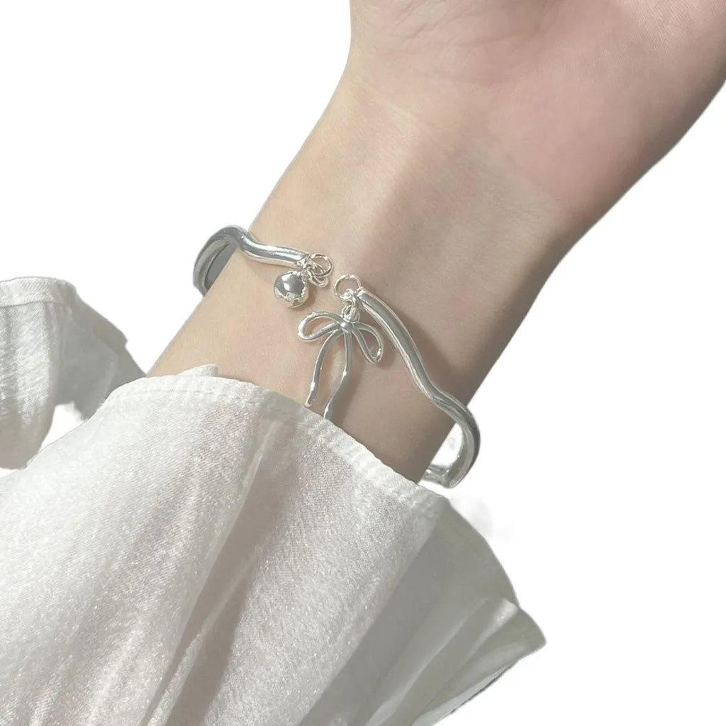 Silver adjustable bracelet with a detailed bow charm on a model's wrist, showing the adjustable clasp.
