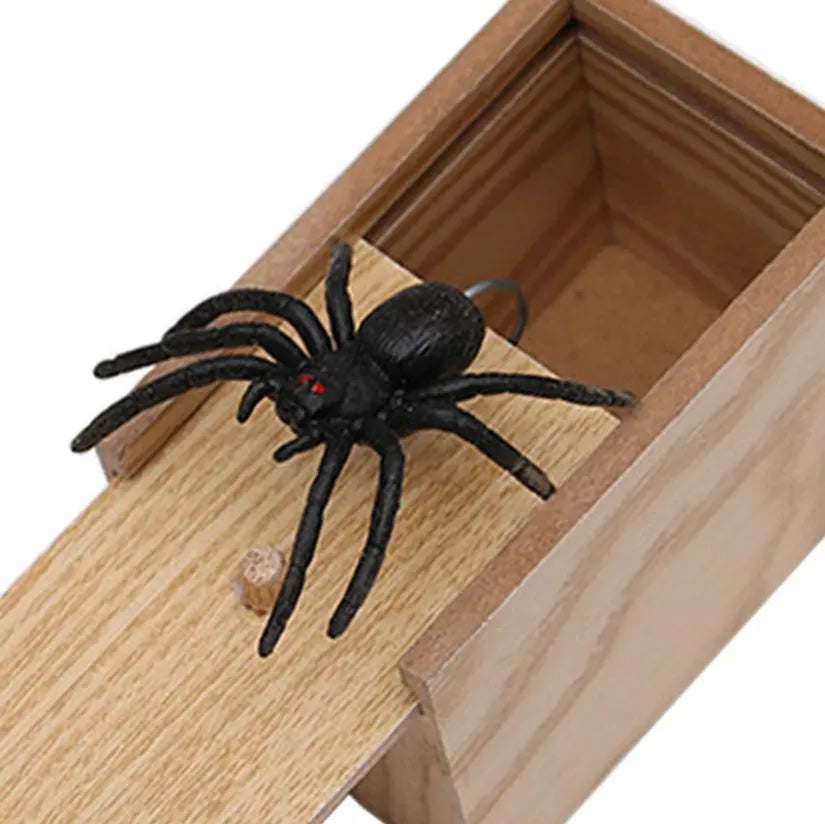 Wooden prank scare box closed, with a lifelike jumping spider toy next to it.