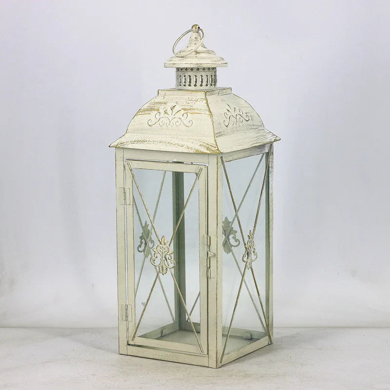Black wrought iron floor-standing storm lantern with clear tempered glass panels on a garden patio.