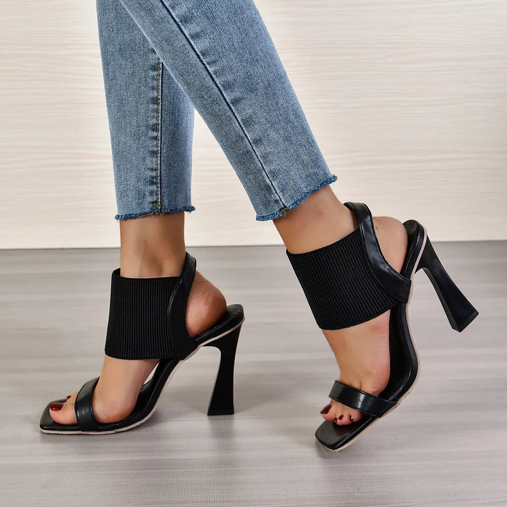 Women's black high heel sandals with a thin elastic ankle strap and a rubber sole.