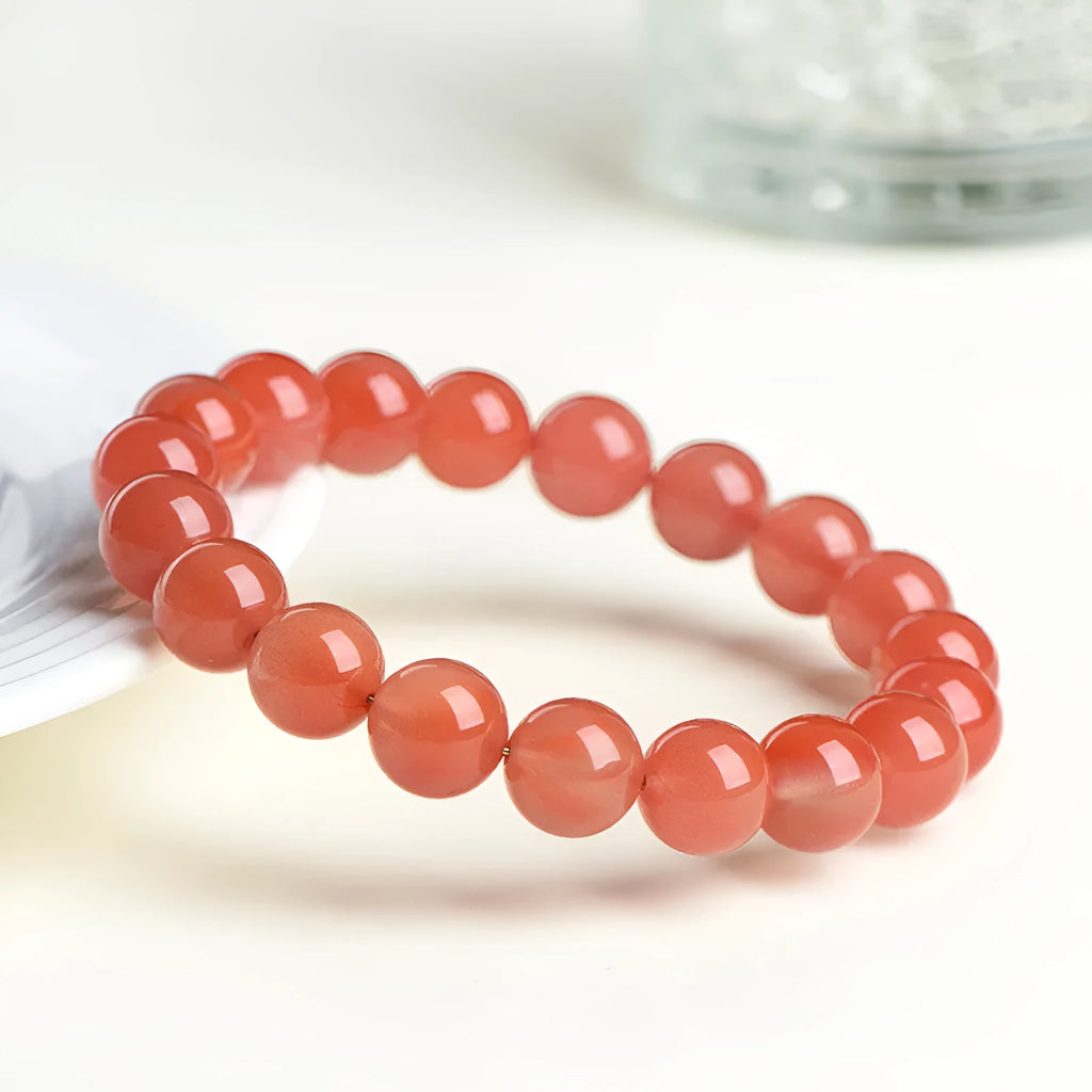 Natural cherry red agate bracelet with hand-polished beads on a wrist, showing colour variation and secure clasp.