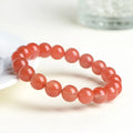 Natural cherry red agate bracelet with hand-polished beads on a wrist, showing colour variation and secure clasp.