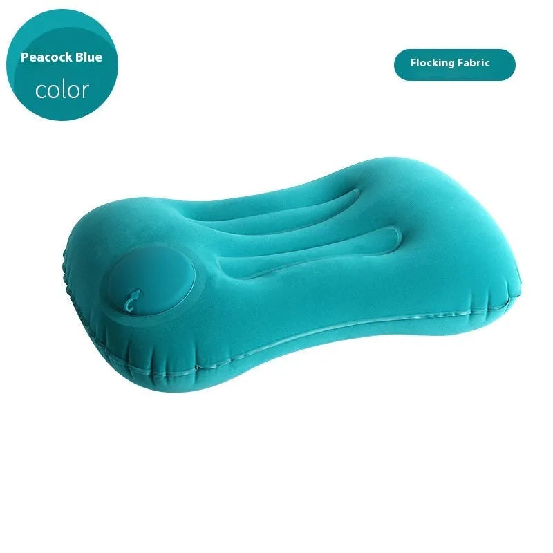 Grey inflatable travel pillow with soft flocking surface, shown deflated and next to a backpack for scale.