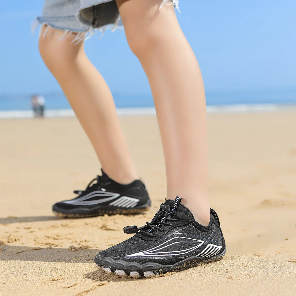 Children's quick-drying water shoes with non-slip rubber soles in multiple colours on a sandy beach.