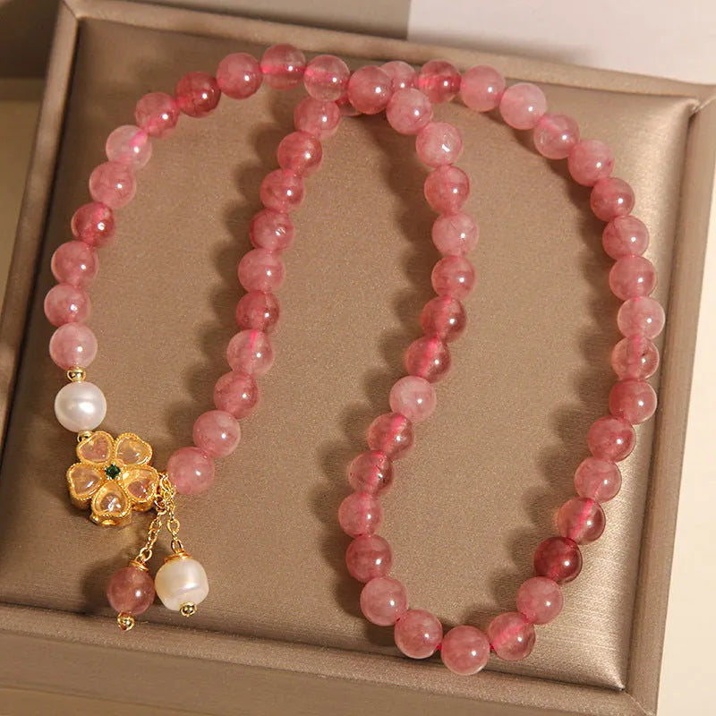 Women's double ring bracelet with strawberry quartz four-leaf clover charms on wrist.